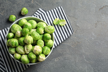 Bowl of fresh Brussels sprouts and napkin on grey background, top view with space for text