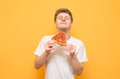 Portrait of a guy in a white T-shirt eats a piece of fresh pizza and gets a pleasure, isolated on a yellow background. Young man is happy to eat a delicious piece of pizza on a yellow background.