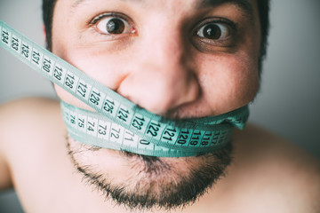 Portrait of bearded frustrated fat man with green measuring tape around his mouth, healthy eating concept