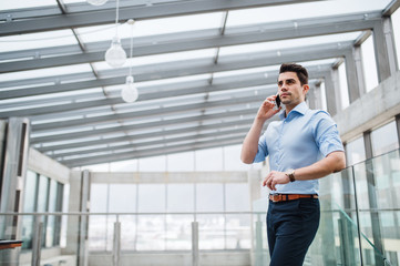 Wall Mural - A low-angle view of young businessman with smartphone in corridor outside office.