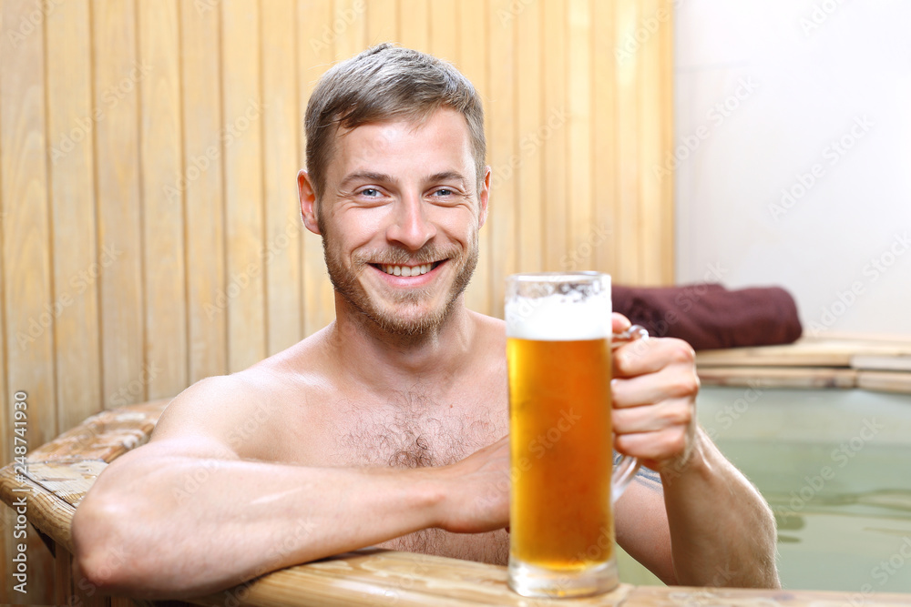 Kąpiel w piwie. Przystojny mężczyzna zażywa kąpieli w bali z woda termalną pijąc piwo kuflowe. - obrazy, fototapety, plakaty 