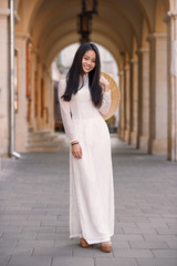 Beautiful happy asian girl dressed in Ao Dai dress with vietnamese conical hat against arches background.