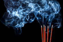 Closeup Of Calmly Burning Incense Sticks With Blue Fume On Black Background
