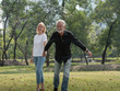 © xreflex - Happy senior man and woman couple walking and holding hands in a park on a sunny day. relax in the forest spring summer time. free time, lifestyle retirement grandparents concept.