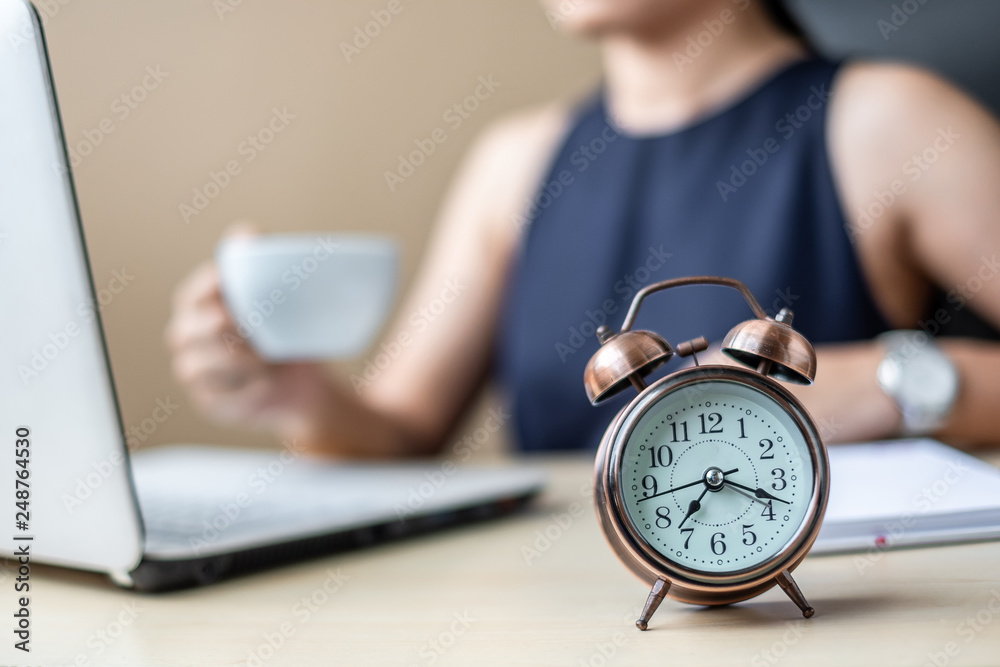 Close up alarm clock with young Businesswoman using laptop analysis marketing plan and drinking coffee in the morning. Business, Finance and lifestyle concepts - obrazy, fototapety, plakaty 