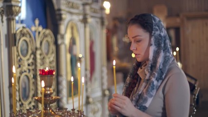 Wall Mural - lifestyle woman lights candles in the Church, praying in front of the icon