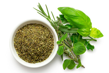 Dried chopped provence herbs in a white ceramic bowl next to fresh bouquet garni isolated on white from above.