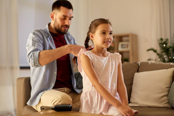 Wall Mural - family and people concept - happy father braiding daughter hair at home in evening