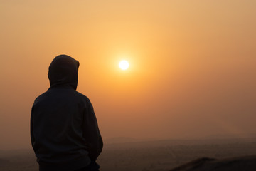 A person weareed hoody sat on the mountain by watching sunset.