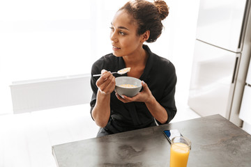 Wall Mural - Portrait of pretty african american woman wearing housecoat, having breakfast at home