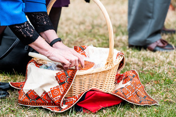 Ukrainian Orthodox Easter blessing wicker straw baskets with senior woman's hand placing candle on grass ground outside at church