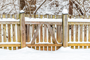 Wall Mural - Wooden fence gate locked covered in white snow after heavy snowing snowstorm storm by house home with forest trees bushes in background in Virginia