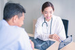© amornchaijj - Woman doctors are explaining something from a tablet to a sick male patient.