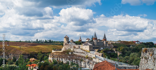 Plakat Stary zamek Kamianets-Podilskyi pod zachmurzonym błękitnym niebem. Twierdza położona wśród malowniczej przyrody w historycznym mieście Kamianets-Podilskyi, Ukraina