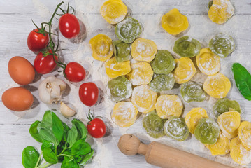 Wall Mural - Homemade fresh Italian ravioli pasta on white wood table  with flour, basil, tomatoes,background,top view.