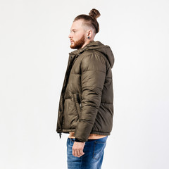 Fashionable man with beard and bun hairstyle dressed in yellow sweater, jeans and brown jacket poses in the studio on the white background. Casual style