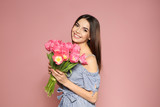 Fototapeta Tulipany - Portrait of beautiful smiling girl with spring tulips on pink background. International Women's Day