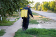 A man in overalls from a sprayer behind his back to spray weeds.  Pest control concept