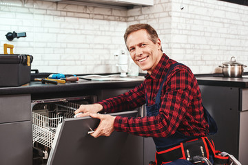 Wall Mural - Call the professional. Male technician sitting near dishwasher and smiling