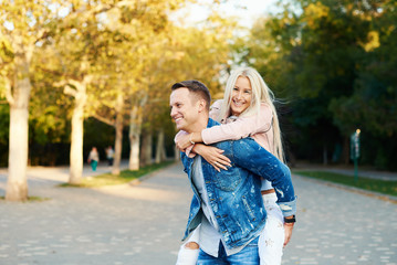 Happy couple on vacation. Lovers are laughing. Happy guy and girl. Lovers enjoy each other in the sunny park. Boyfriend carrying his girlfriend on piggyback