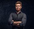 © Fxquadro - Smiling elegantly dressed redhead man posing with his arms crossed in studio against a dark textured wall