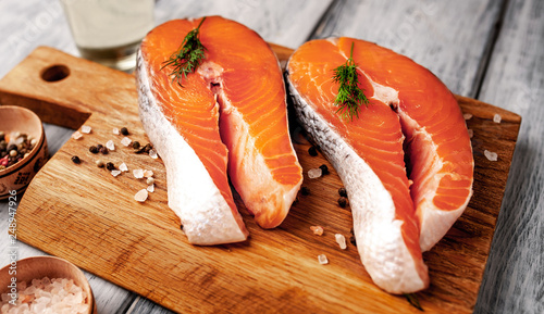 Fotografía Raw salmon steaks with spices, herbs, salt and lemon on a wooden table backgroun