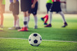 © Koonsiri - soccer ball on green artificial turf with blurry soccer players standing