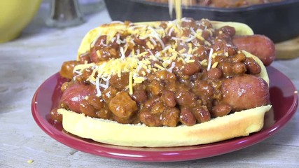 Canvas Print - Sprinkling grated cheddar cheese on a hot dog smothered in chili 