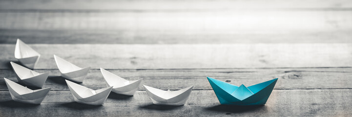 blue paper boat leading a fleet of small white boats on wooden table with vintage effect - leadershi
