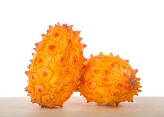 Two whole Kiwano fruit, also known as Cucumis metuliferus, horned melon, or African horned cucumber sitting on wood table isolated on white. Kiwano is a traditional food plant in Africa.