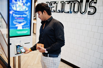 Indian man customer at store place orders and pay by contactless credit card on mobile phone through self pay floor kiosk for fast food, payment terminal. Pay pass.