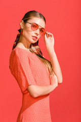 fashionable model posing in living coral dress and sunglasses on red background