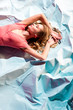 © LIGHTFIELD STUDIOS - top view of attractive woman in elegant living coral dress lying on light blue crumpled paper