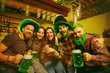 Saint Patrick's Day Party. Happy friends is celebrating and drinking green beer. Young men and women wearing a green hats. Pub Interior.
