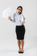 Wall Mural - Full length photo of irritated businesswoman wearing eyeglasses holding paper folders in the office, isolated over white background