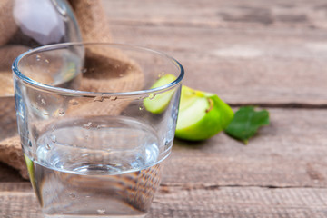 Dietary detox drink with apple slices in clean water and a fresh apple on a wooden table, close up