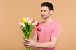 © LIGHTFIELD STUDIOS - handsome man looking at bouquet of tulips isolated on beige
