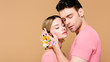 © LIGHTFIELD STUDIOS - handsome man with alstroemeria flowers on hand touching face of attractive girlfriend isolated on beige