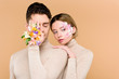 © LIGHTFIELD STUDIOS - man with alstroemeria flowers on hand covering one eye near beautiful woman with flowers on face isolated on beige