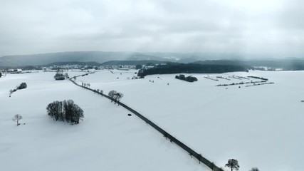 Wall Mural - Aerial shot of a lonely road winding trough the snow on a cloudy winter day. Drone moves along road, street