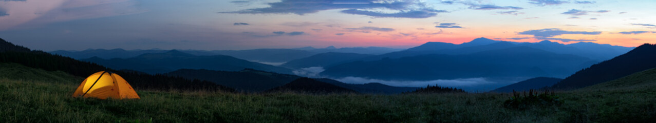 Wall Mural - orange tourist tent illuminated from inside stands in mountains above clouds