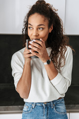 Wall Mural - Image of happy african american girl drinking tea, while standing in bright flat