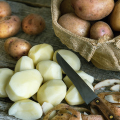 Wall Mural - Peeled potatoes ,kitchen knife, potato peels and a burlap sack of unpeeled potatoes on the wooden boards