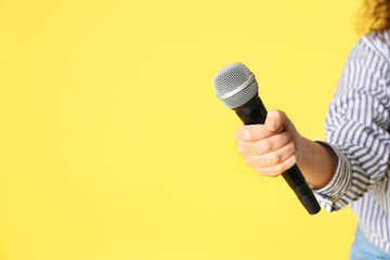 Young woman holding microphone in hand on color background. Space for text