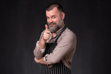 Mature bearded man in apron pointing with finger at camera