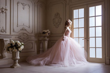 Beautiful Young Blond Woman In Luxurious Long Pink Dress Posing In Vintage Room Interior. Indoor Studio Shot.