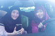 Two Muslim women travelling in the car, looking the way at the smartphone