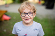 Blonde smiling boy with strabismus wearing glasses with special lens in warm park
