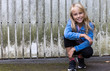 © Westend61 - Portrait of smiling blond girl crouching in front of wooden wall