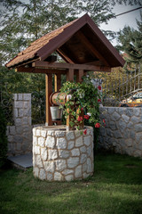 Stone well with a wooden roof and a bucket of water in beautifully modern garden